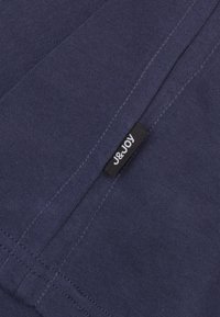 Navyblauwe stof met een gladde textuur, voorzien van zichtbare stikdetails en een zwart label met witte tekst met het label "J&JOY."