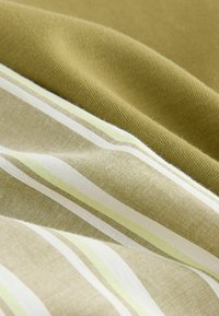 Audinys su dryžuota raštais alyvuogių žalia, grietinėlės ir pastelinių geltonų atspalvių. Minkšta tekstūra su persidengiančiais sluoksniais, pabrėžiančiais skirtingas audinio svorio savybes.