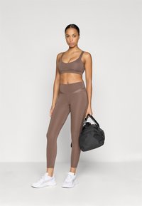Sutien sport și colanți maro, realizați dintr-un material elastic. Asortați cu adidași albi și o geantă de sport neagră. Design simplu, cu accente minime.