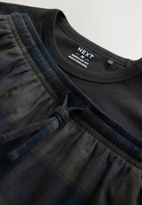 T-shirt nera con scollatura rotonda abbinata a pantaloni da pigiama a fantasia a scacchi, caratterizzati da un elastico in vita e un cordoncino nei colori scuri.
