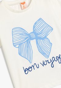 Biała bawełniana koszulka dziecięca z niebieskim paskowanym wzorem w kształcie kokardy oraz haftem "bon voyage" w ciemnoniebieskim kolorze na dole.