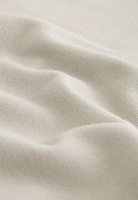Tessuto beige morbido con una trama a maglia fine, che mostra pieghe delicate e superficie liscia.