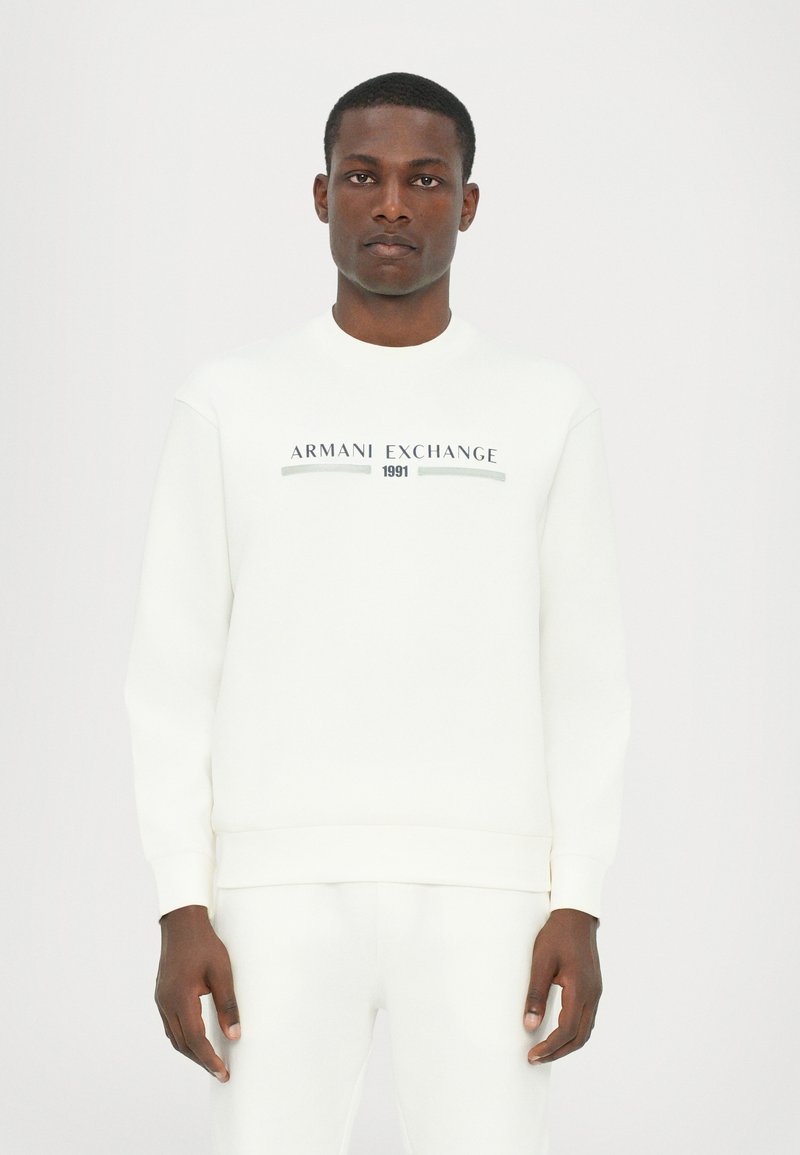 Fehér pulóver, amelyen a "ARMANI EXCHANGE 1991" felirat található fekete és szürke színben. Rugalmas mandzsetták és alsó szegély, puha anyag, minimalista dizájn.