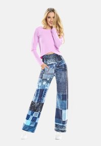 Hosszú ujjú rózsaszín cropped top, széles lábú kék farmer patched nadrággal, amely különböző árnyalatokat és textúrákat tartalmaz, oldalsó zsebekkel.