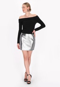 Top lungo nero senza spalle abbinato a una minigonna metallica argento. La modella indossa tacchi neri con cinturini e orecchini circolari.