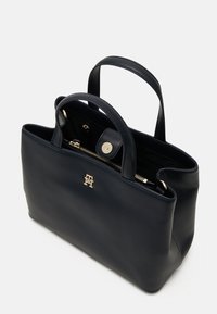 Marineblaue Ledertasche mit doppelten Griffen, goldenem Zubehör, einem Reißverschluss oben und einer Innenreißverschlusstasche. Mit Logodetail auf der Vorderseite.
