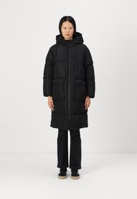 Mustat, polvipituiset toppatakki huppulla, etuvetoketjulla, kaksi suurta etutaskua ja rintatasku. Pehmeä rakenne ja paksu eristys.