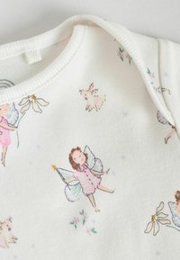 Body din bumbac crem cu mânecă lungă, decorat cu un imprimeu jucăuș cu zâne, rochii roz, flori și animale mici pe un fundal texturat.