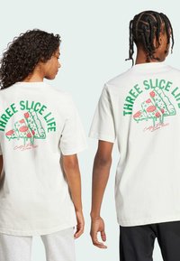 Crèmekleurige t-shirts met een grafische print van pizzapunten in felle kleuren op de achterkant. Losse pasvorm, korte mouwen en een eenvoudige ontwerp aan de voorkant.