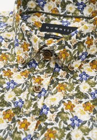 Blumen kurzarmhemd aus weicher Baumwolle mit einem weißen Grund. Es hat gelbe, blaue und orangefarbene Blumen, braune Knöpfe und einen klassischen Kragen.