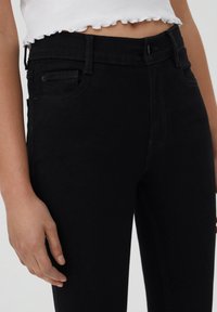 Černé džíny z denimu s úzkým střihem. Mají přední kapsy, poutka na pásek a zapínání na zip. Tkanina má hladkou strukturu.