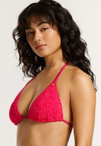 Roze driehoekige bikini top met een gestructureerd bloemmotief, dunne bandjes en een klein gouden logo accent aan de zijkant. Zachte stofafwerking.