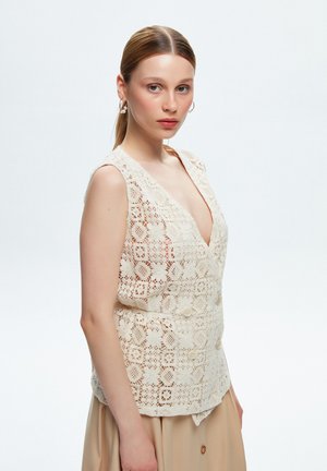Gilet in pizzo all'uncinetto color crema, con scollatura a V profonda, design senza maniche, dettagli con bottoni e motivi floreali intricati.