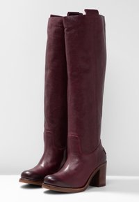 Burgundyröda knähöga läderstövlar med en slät yta, rund tå, chunky träklack och dragflikar för enkel användning.