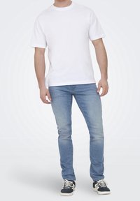 Vit bomullst-shirt, korta ärmar, rund halsringning, kombinerad med ljusblå smala jeans och svarta sneakers med vita sulor och snören.