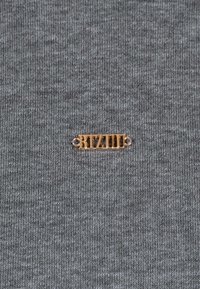 Szary prążkowany materiał z metalową plakietką logo w kolorze złotym z napisem "BIZUU" oraz małymi dekoracyjnymi akcentami po obu stronach.