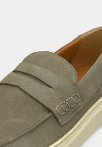 Grønne loafers i ruskind med lagdelt remdesign, beige gummisål og teksturerede syningsdetaljer. Indersiden er i en kontrastfuld orange farve.