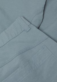 Close-up of light blue fabric with detailed stitching and a belt loop, showing texture and seam lines.