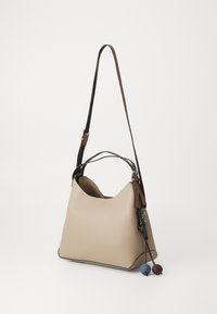 Borsa a spalla in pelle beige dalla forma morbida, con tracolle nere e marroni, e pompon decorativi blu e marroni attaccati.