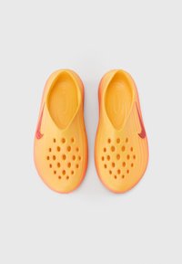 Κίτρινα και πορτοκαλιά παπούτσια χωρίς κορδόνια με υφή, πολλαπλές οπές αερισμού και ροζ σήμα Nike στο πλάι.