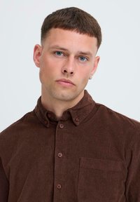 Brown corduroy shirt with a button-down collar, long sleeves, front pocket, and button closures. Fabric features vertical ribbing texture.
