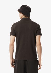 Brun polo tröja med smal passform, korta ärmar och klassisk krage. En ribbad textur är synlig, ihop med matchande mörka shorts och en svart bucket hat.