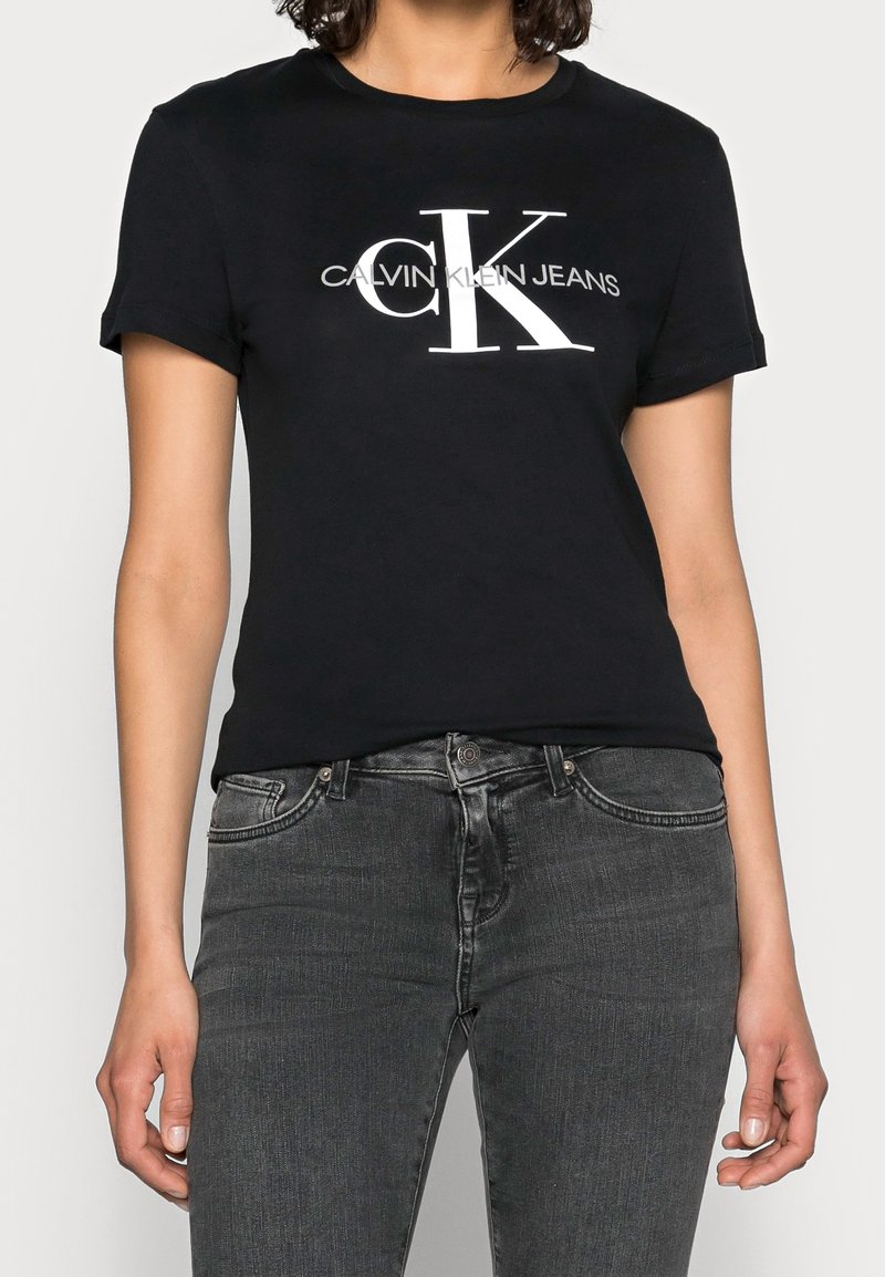 Svart bomullströja med rundad halsringning och korta ärmar, med en vit "CK"-logotyp och texten "CALVIN KLEIN JEANS" centrerad på framsidan.
