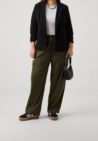 Černé sako, bílý top, olivově zelené cargo kalhoty, černé boty s bílými pruhy a malá černá kabelka. Elegantní, ležérní prvky outfitu.