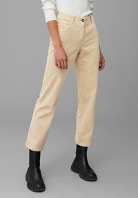 Beige corduroy broek met een recht model, voorzien van steekzakken en een enkele knoopsluiting, gecombineerd met zwarte enkellaarsjes.