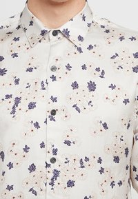 Light fabric shirt with a white base, featuring a floral pattern in purple and red. Classic collar and button front closure.