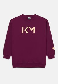 Felpa bordeaux con un grande logo beige "KM" sul davanti e dettagli arancioni testurizzati sulle maniche. Polsini e fondo elastici.