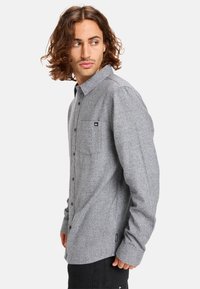Gray flannel shirt with a button-down collar, single pocket, and subtle texture. Features a small logo and standard fit design.