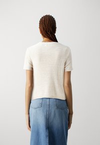 Strickpullover in Creme mit kurzen Ärmeln und rundem Ausschnitt, strukturiertem Finish, kombiniert mit einem hellblauen Jeansrock mit Gesäßtaschen.
