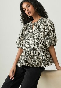 Peplum top i beige med sorte zebra-striber; har en nøglehul-udskæring og puffy ærmer. Struktureret stof; parret med sorte bukser.