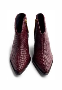 Bottes chelsea en cuir bordeaux avec un motif tissé texturé, bouts pointus et accents en zip doré sur les côtés. Doublure intérieure noire.