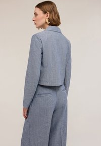 Veste ajustée à rayures bleues avec manches longues, revers en pointe, design court et tissu texturé. Portée avec un pantalon taille haute assorti.