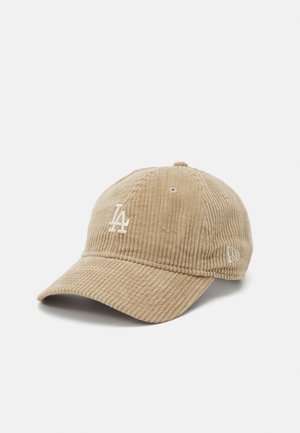 Casquette de baseball en velours côtelé beige avec une visière incurvée, ornée d'un logo brodé blanc sur le devant et d'un petit emblème sur le côté.