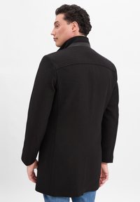 Schwarzer Wollmischmantel mit strukturiertem Kragen, langen Ärmeln und tailliertem Schnitt. Verfügt über eine dezente Textur und klare Linien im Design.