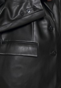 Sort læderjakke med en glat tekstur, struktureret design, fire knapper og detaljeret brystlomme.