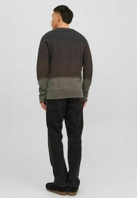Donker gradient sweater met geribbelde manchetten en onderrand, overgaand van donkerbruin naar grijs. Gecombineerd met zwarte broeken en donkere schoeisel.