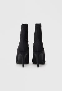 Czarne, wysokie botki na obcasie wykonane z miękkiego, elastycznego materiału. Charakteryzują się smukłym kształtem, gładką fakturą oraz cienkim, eleganckim obcasem.