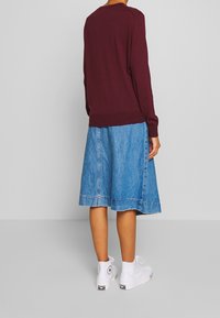 Vinröd tröja med långa ärmar, matchad med en ljusblå jeanskjol och vita höga sneakers, som har en fransig fåll och subtila sömmar.