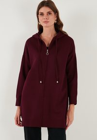 Bordo užtrauktuku užsisegantis džemperis su kapu, ilgomis rankovėmis ir raišteliais; pasižymi tekstūruota medžiaga ir priekiniais užtrauktukais, užtikrinančiais komfortą.