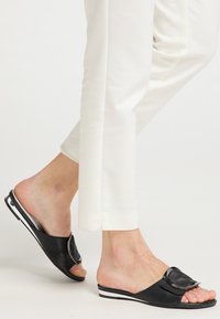 Infradito nere in pelle liscia, caratterizzate da una larga fascia con una fibbia lucida e una suola a strisce bianche. Indossate con pantaloni bianchi.