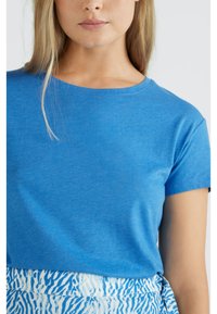 Camiseta azul de manga corta hecha de tela suave, con un cuello redondo clásico y una textura lisa, combinada con una falda estampada.