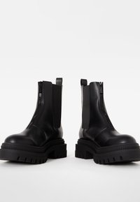 Černé kožené kotníkové boty se zipy na boku, elastickými panely, silnou kaučukovou podrážkou a texturovanými designy pro zvýšenou přilnavost a odolnost.