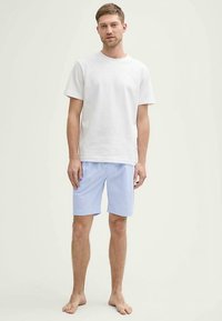 Weißes Baumwoll-T-Shirt kombiniert mit hellblauen, vertikal gestreiften Shorts. Beide Kleidungsstücke sind locker geschnitten und aus atmungsaktivem Stoff gefertigt.