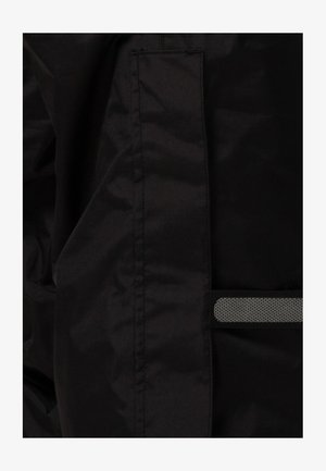 Schwarzer Stoff mit einer glatten Textur verfügt über eine genähte Tasche und einen reflektierenden Streifen. Das Design ist praktisch und funktional für den Einsatz im Freien.