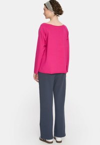 Fuksjowa bluzka z długim rękawem i szerokim dekoltem, w połączeniu z luźnymi, ciemnoszarymi spodniami i białymi butami, o prostym, czystym designie.