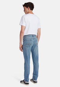 Jeans in denim azzurro chiaro con vestibilità dritta, design a cinque tasche e dettagli di cucitura sottili, indossati con una t-shirt bianca semplice.